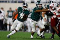 Michigan State's Kenneth Walker III, left, rushes against Nebraska's Caleb Tannor, right, as Mi ...