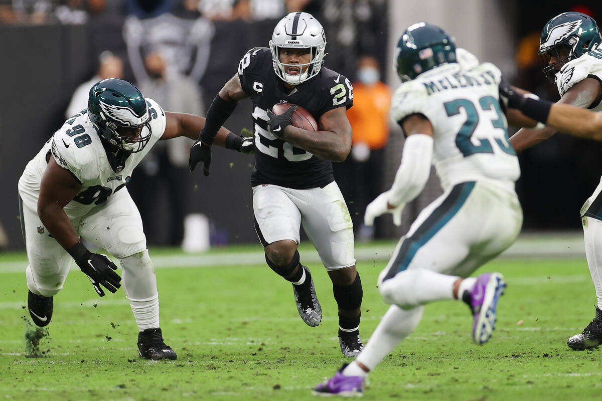 Raiders running back Josh Jacobs (28) runs the ball under pressure from Philadelphia Eagles def ...
