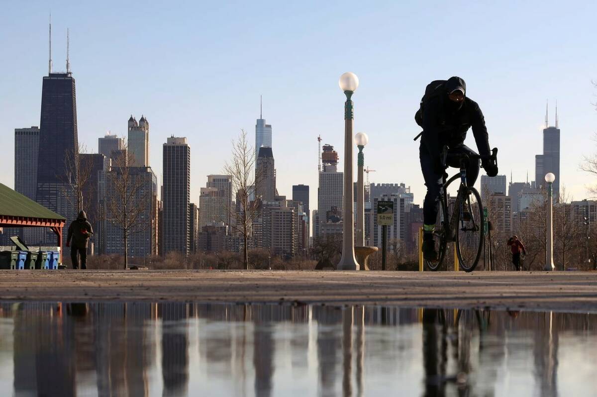 The Chicago skyline is reflected in the water of the thawed snow as a cyclist passes by at Nort ...
