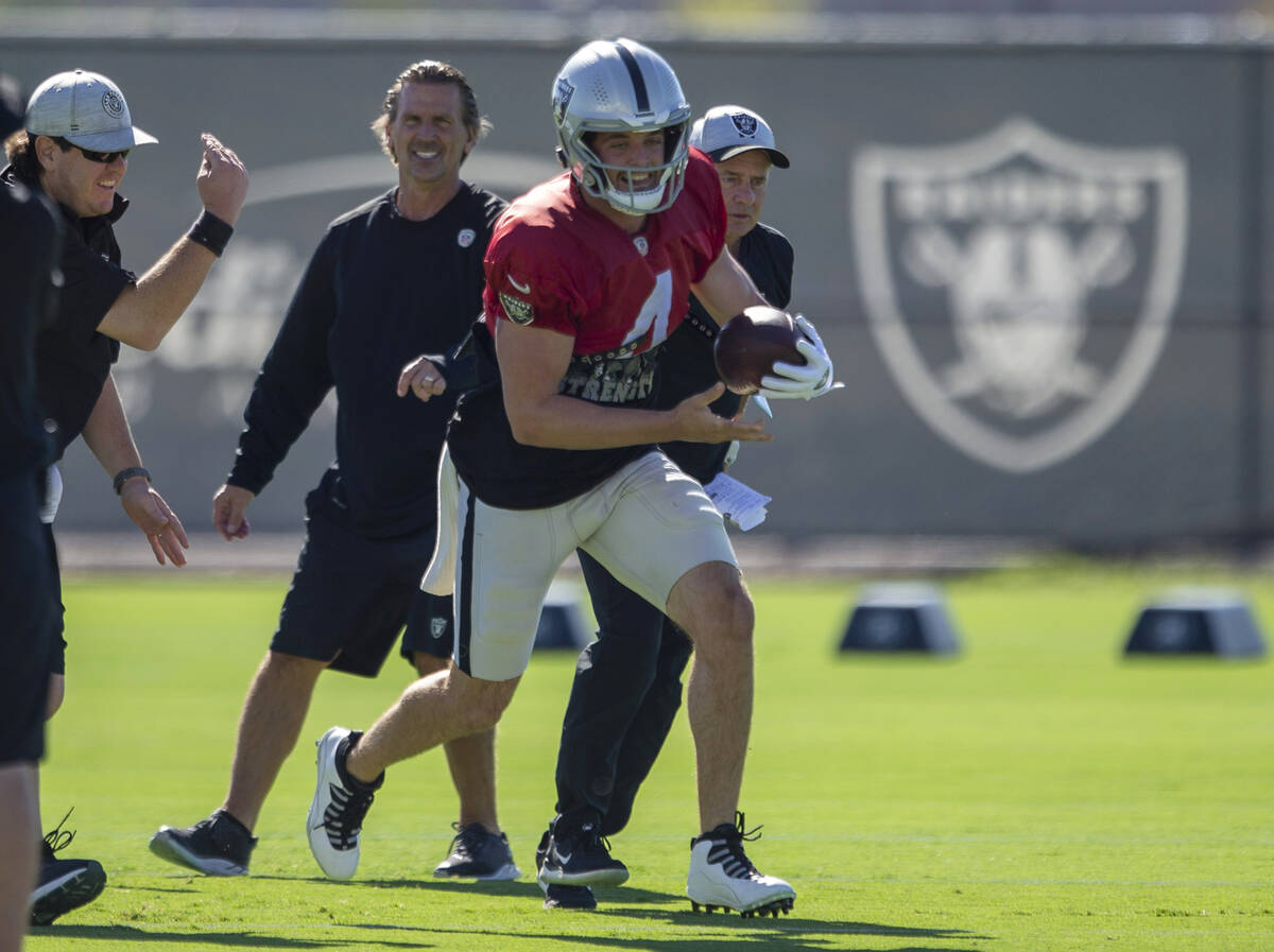 Raiders quarterback Derek Carr (4) smiles as he carries the football with Raiders offensive coo ...