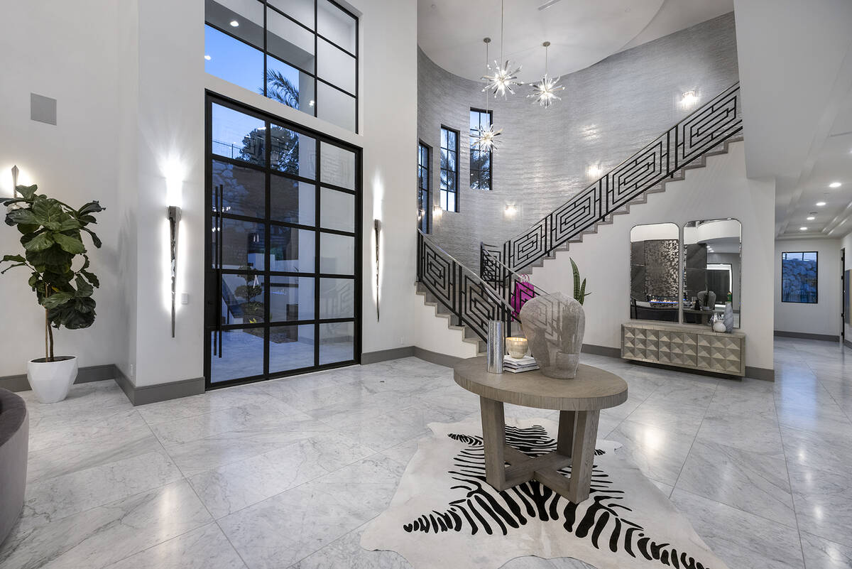 The property’s dramatic entry unfolds through a stately custom glass-and-black metal door fla ...