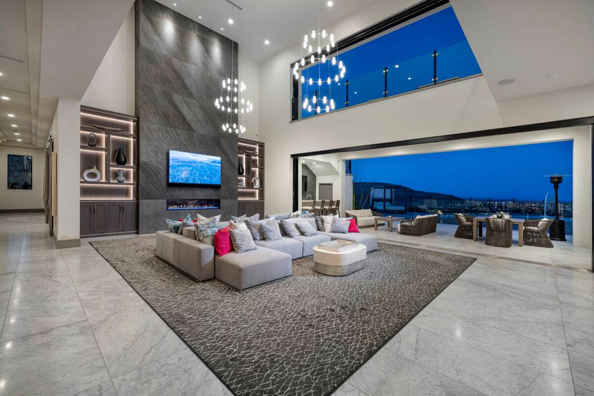 The two-story great room features custom built-ins with ambient lighting bordering a central fi ...