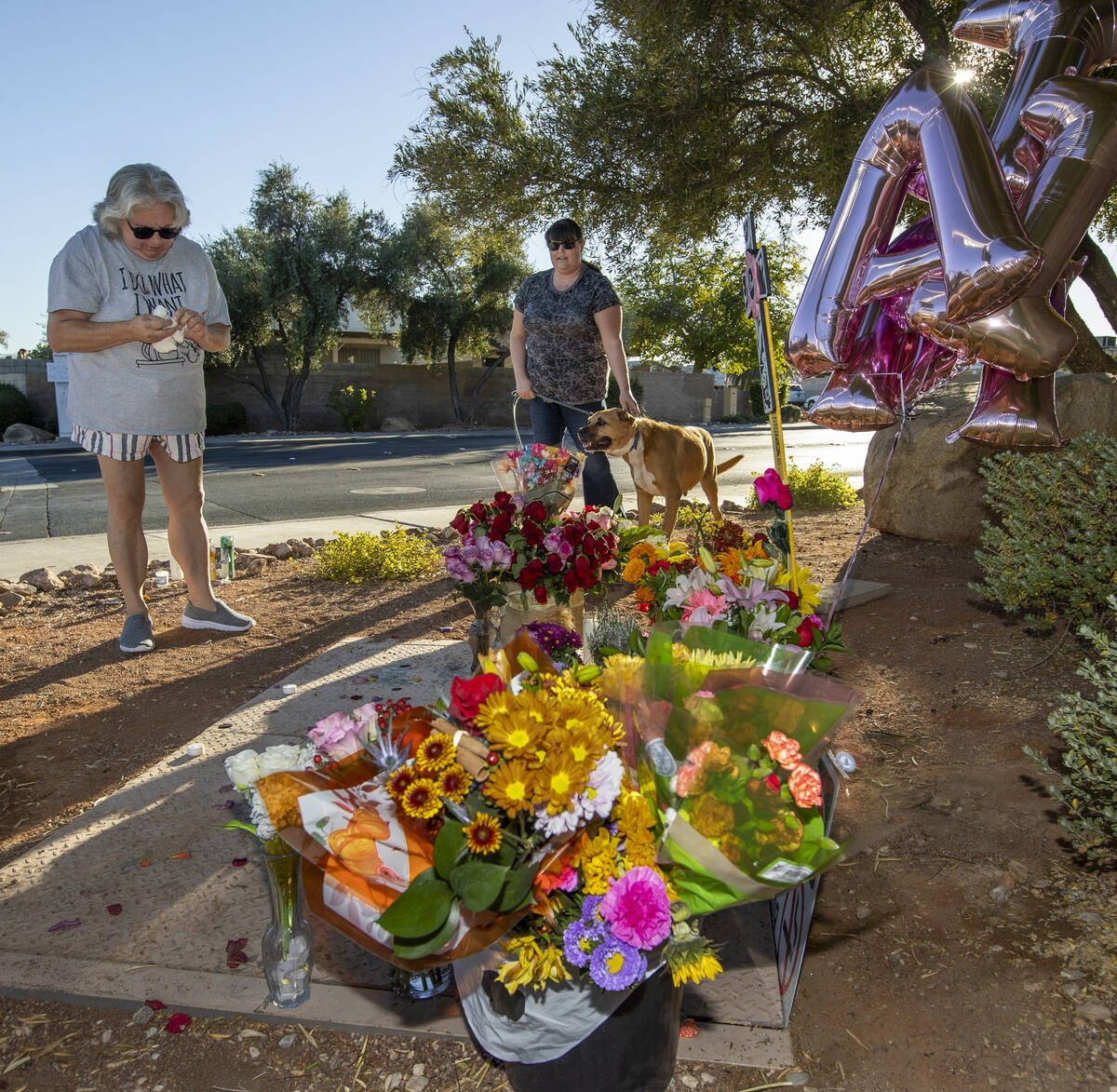 From left, Linda and Megan Bendon with dog Rhett stop to light a candle and leave a stuffed dog ...