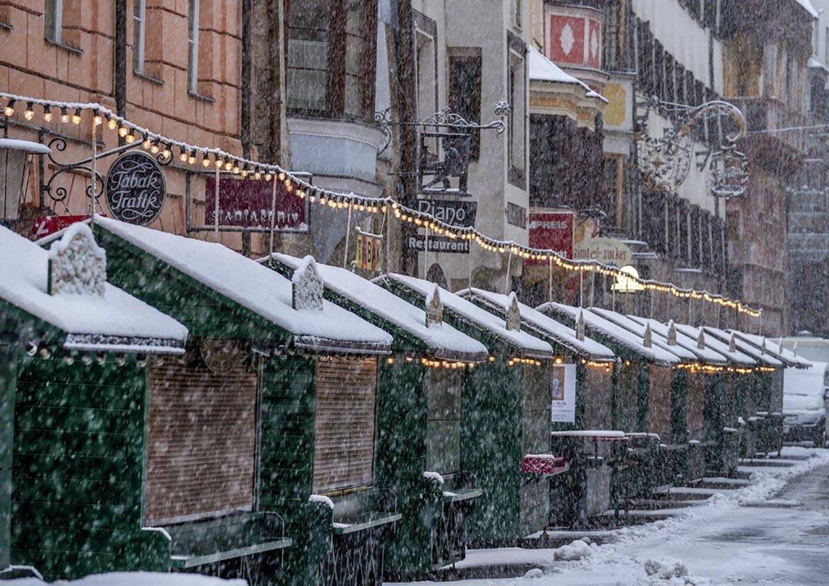 Christmas booths are all closed on the Christmas market in Innsbruck, Austria, as snow falls on ...