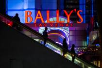 People are silhouetted by a sign for Bally's as they descend an escalator from a pedestrian bri ...