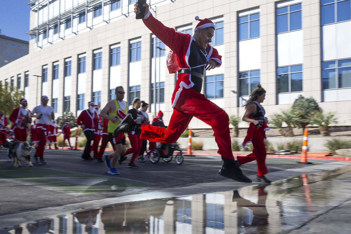 A runner leaps over a puddle during The Las Vegas Great Santa Run on Saturday, Dec. 4, 2021, in ...