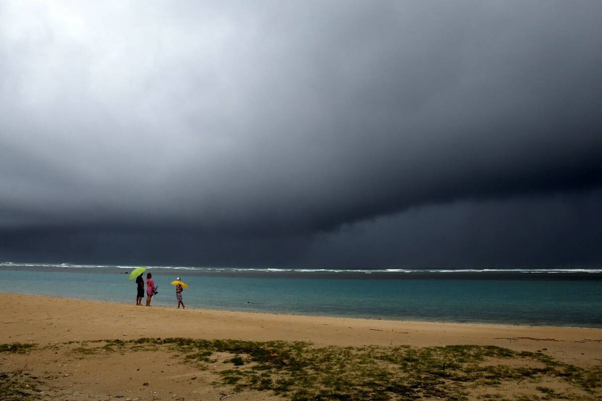 People hold umbrellas as it begins to rain on an otherwise empty beach in Honolulu on Monday, D ...