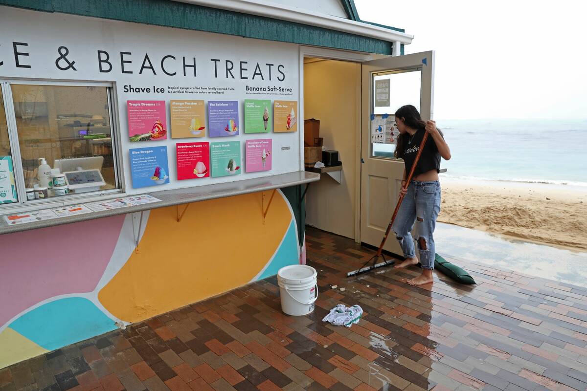 Calista Cafiero sweeps storm water out of the shop she manages on Waikiki Beach, Monday, Dec. 6 ...