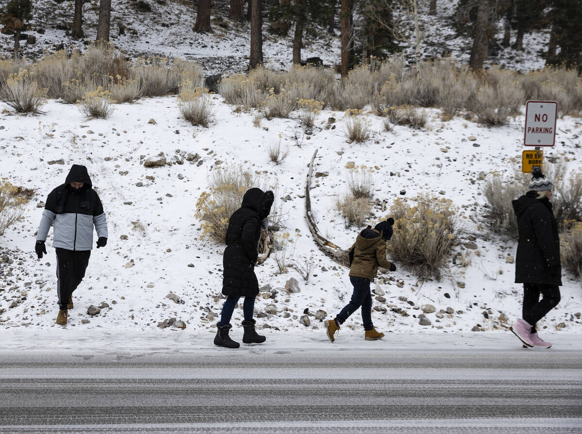 People walk along snow covered road as light snow fall on the Mt. Charleston area on Thursday, ...