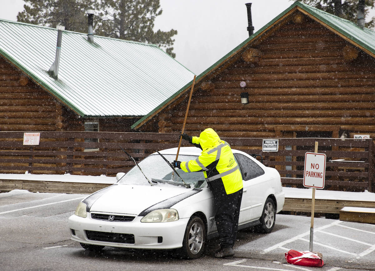 A worker at the Mt. Charleston Lodge cabins removes snow from a parked car as light snow fall o ...