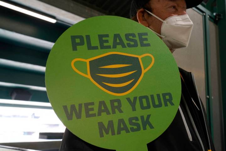 A stadium worker holds up a sign for people to wear face masks before a game between the Oaklan ...