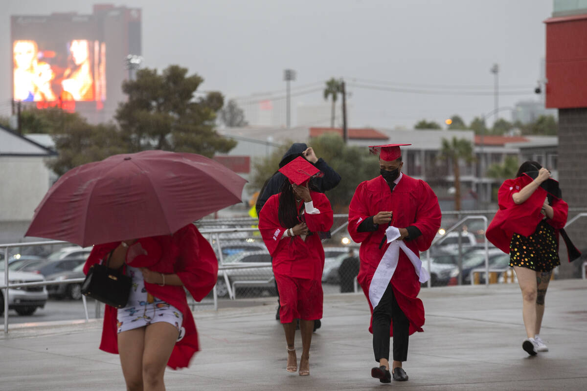 UNLV graduates shield themselves from wind and rain as they walk into their graduation ceremony ...