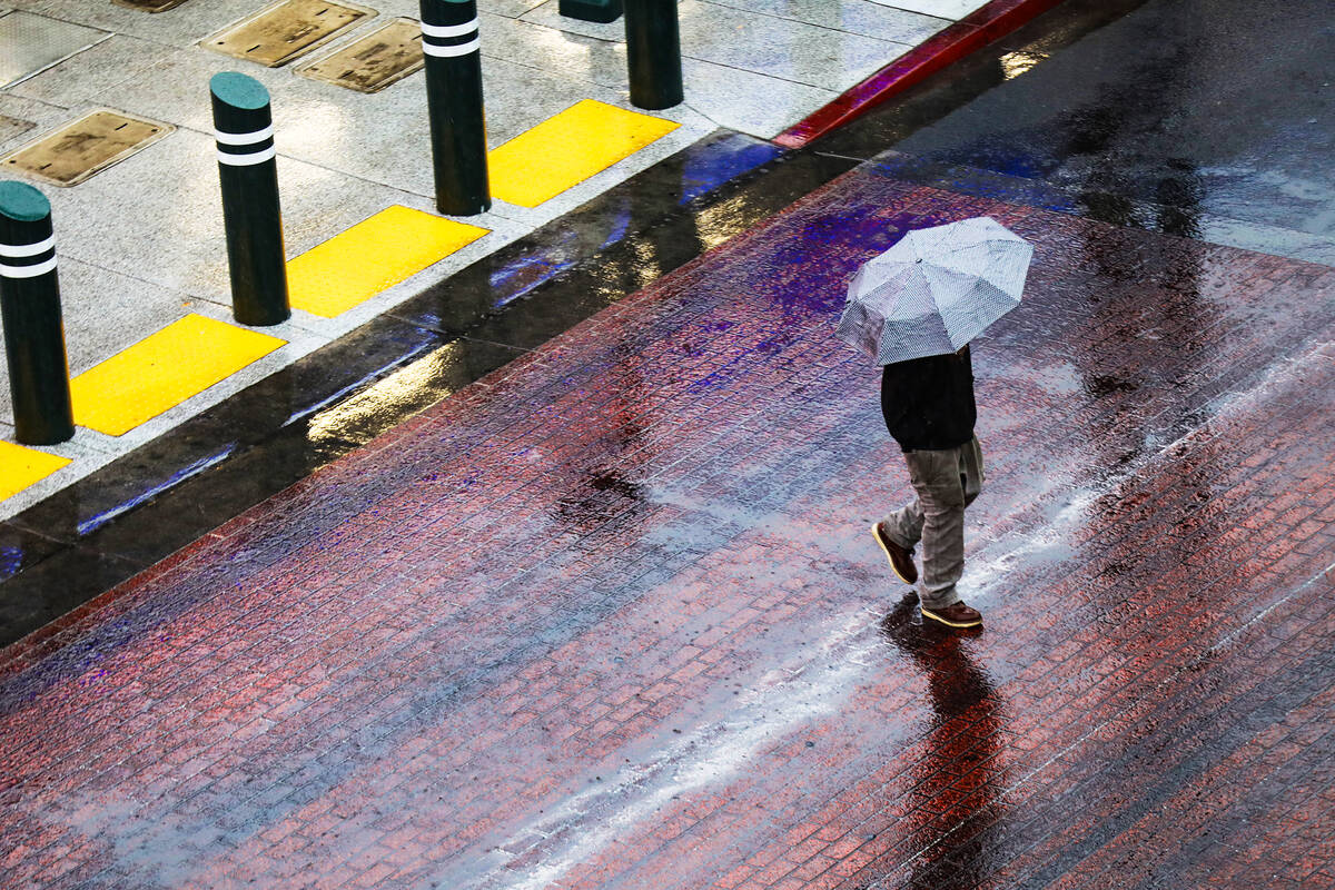 A man walks through the rain at the Fremont Street Experience in Downtown Las Vegas, Tuesday, D ...