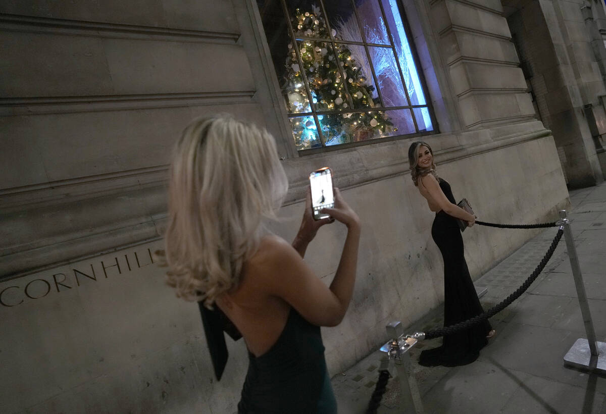 Two women dressed for a party take photos of each other outside a venue in London, Friday, Dec. ...