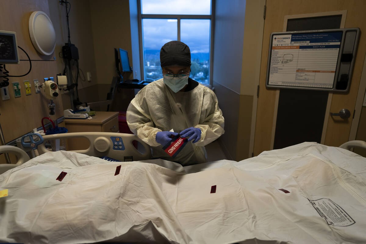 Registered nurse Bryan Hofilena attaches a "COVID Patient" sticker on a body bag of a ...