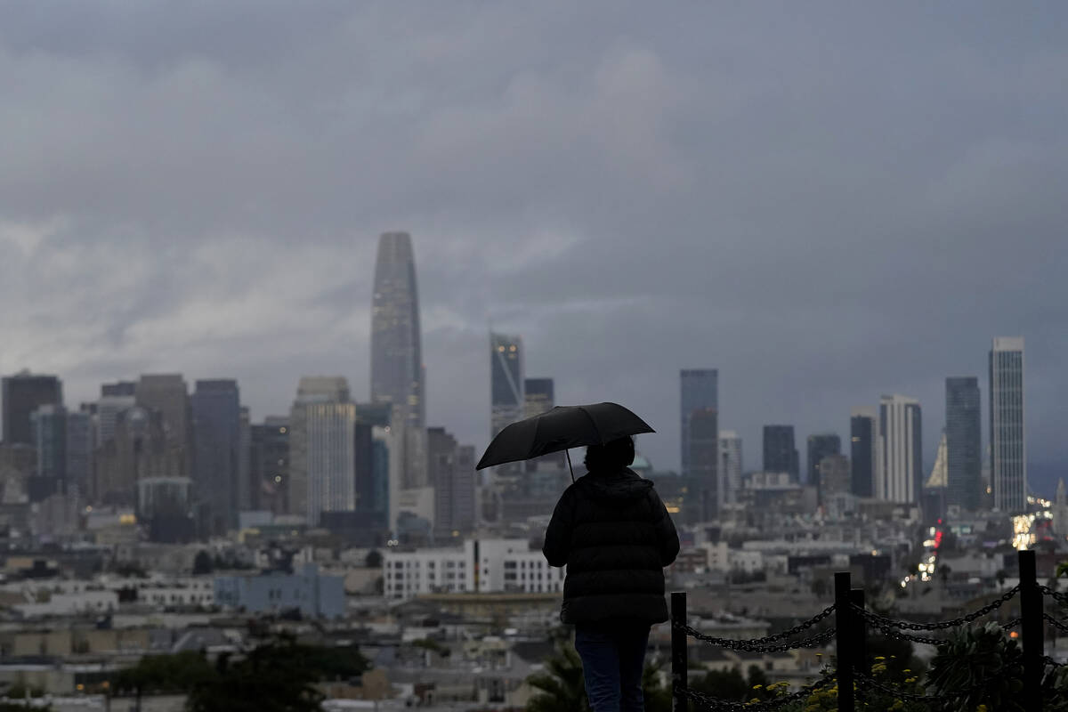 A pedestrian carries an umbrella while looking toward the skyline from Dolores Park in San Fran ...