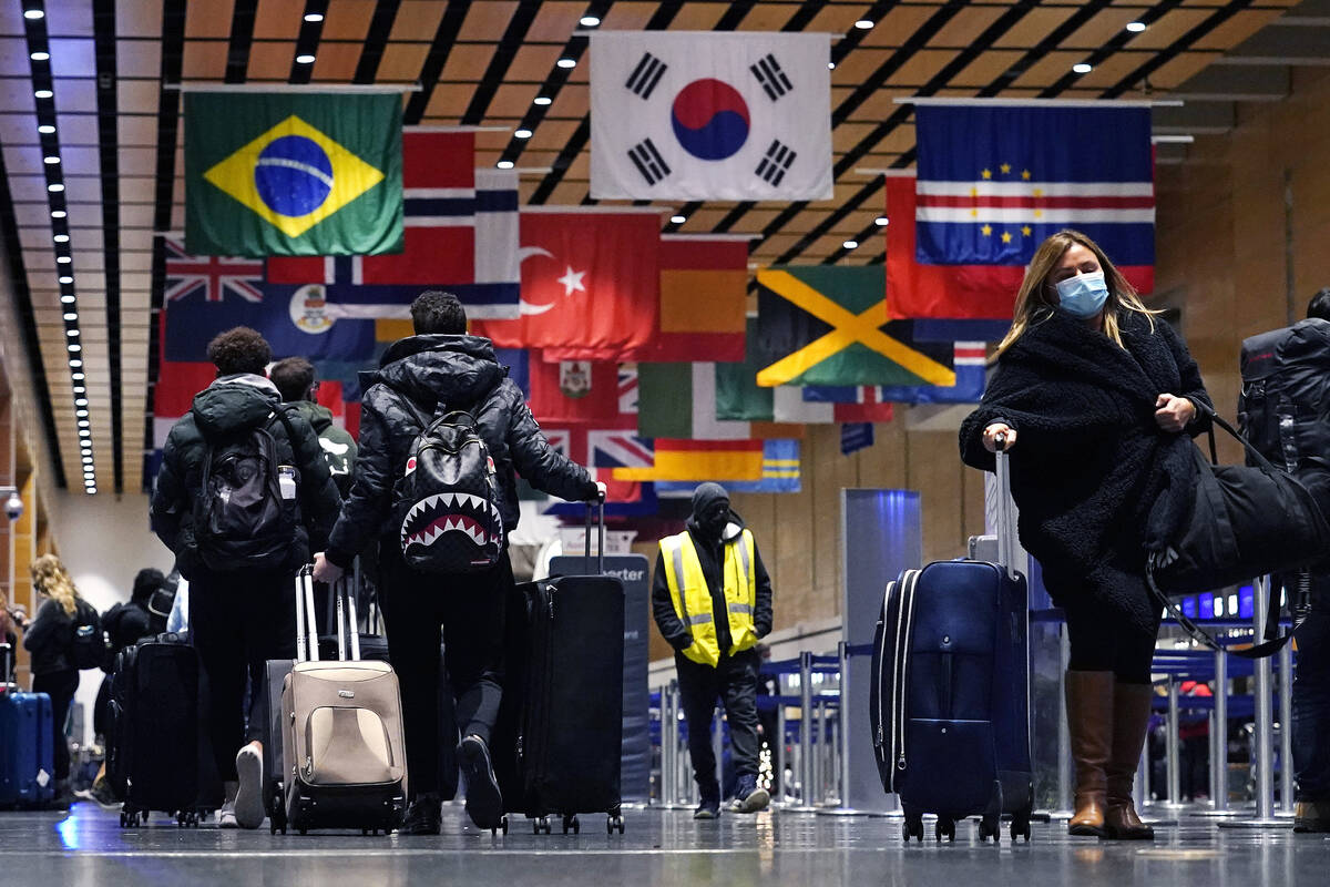 Travelers trek through Terminal E at Logan Airport, Tuesday, Dec. 21, 2021, in Boston. At leas ...