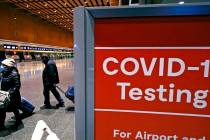 Travelers pass a sign near a COVID-19 testing site in Terminal E at Logan Airport, Tuesday, Dec ...