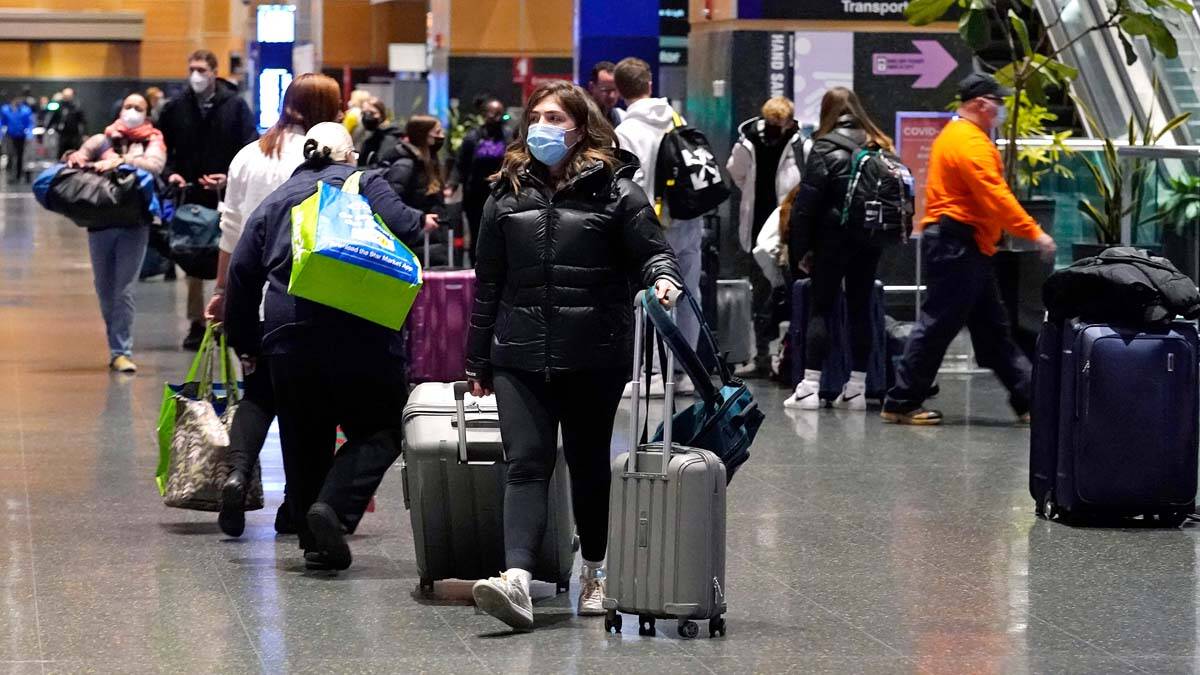 Travelers trek through Terminal E at Logan Airport, Tuesday, Dec. 21, 2021, in Boston. At leas ...