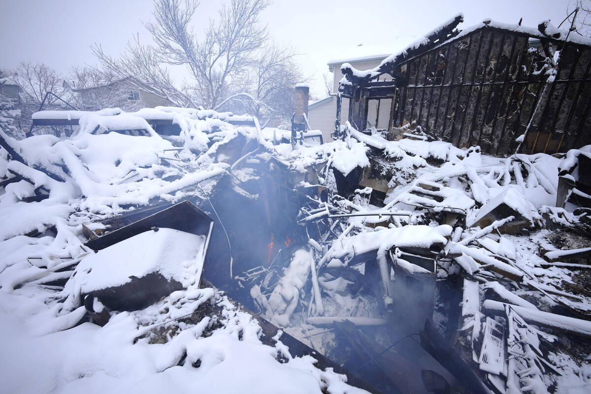 A lone flame flickers as smoke roils from the remains of a home destroyed by a pair of wildfire ...