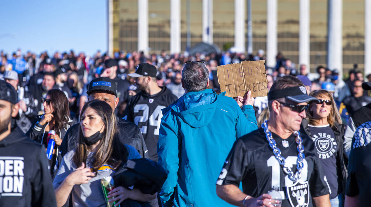 A man holds up a sign looking to buy tickets as fans stream across the Hacienda Avenue bridge b ...