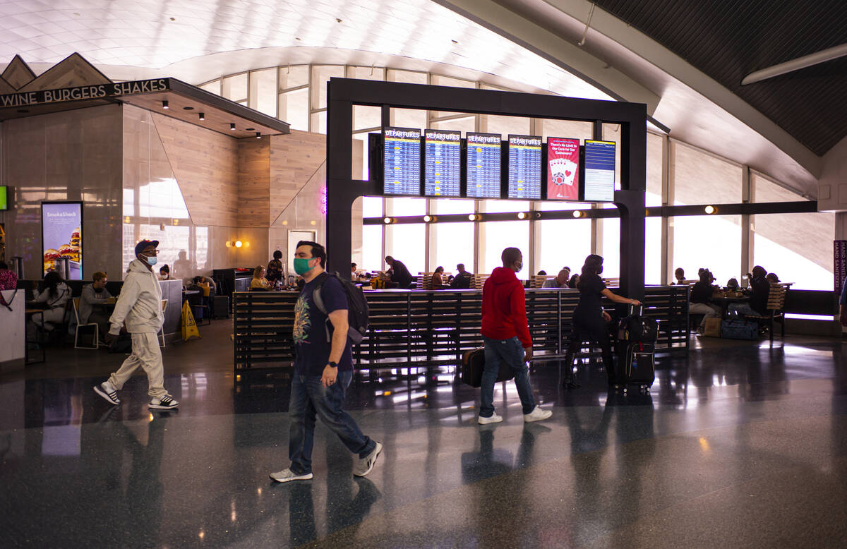 Travelers walk by a display listing departures in Terminal 1 at Harry Reid International Airpor ...