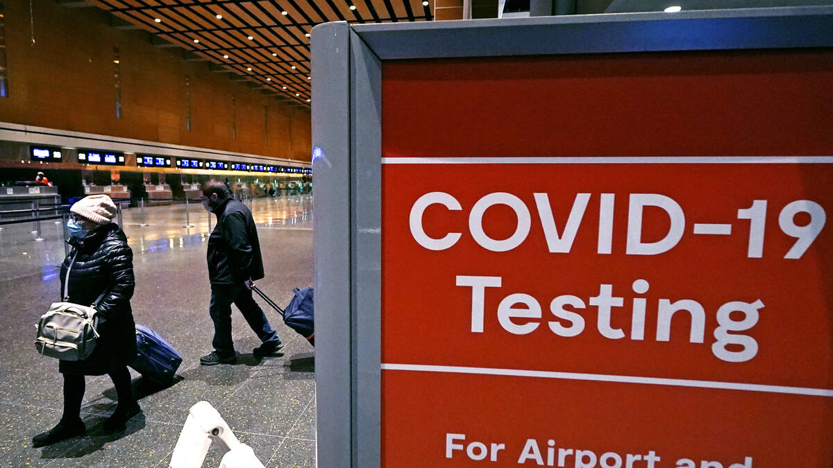FILE - Travelers pass a sign near a COVID-19 testing site in Terminal E at Logan Airport, on De ...