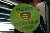 A stadium worker holds up a sign for people to wear face masks before a game between the Oaklan ...