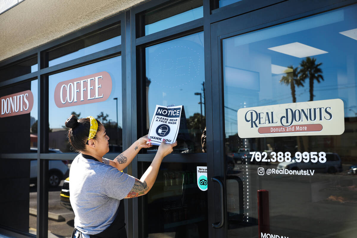 Saige Molina, manager at Real Donuts, takes down a mask mandate sign on Thursday, Feb. 10, 2022 ...