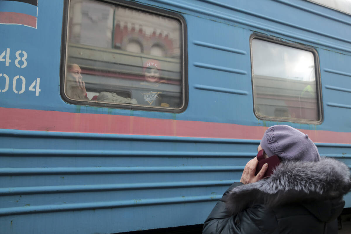 A woman speaks on the phone with her relatives as a child looks through a train window prior to ...