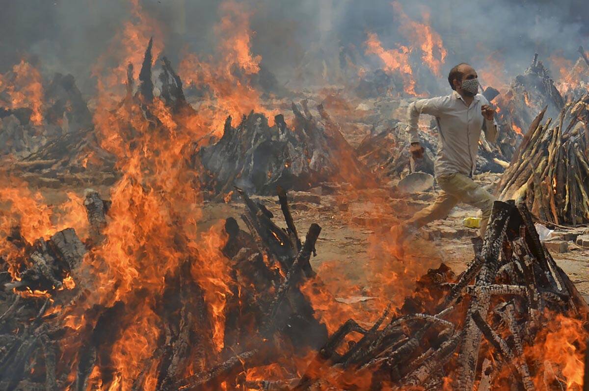 FILE - A man runs out of the heat emitting from the multiple funeral pyres of COVID-19 victims ...