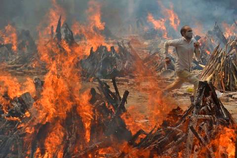 FILE - A man runs out of the heat emitting from the multiple funeral pyres of COVID-19 victims ...