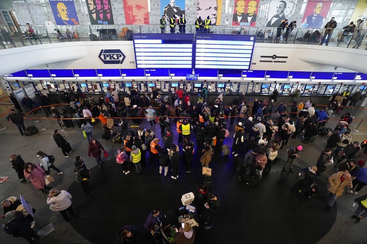 People, some who have fled Ukraine, line up at a ticket counter at the train station in Warsaw, ...