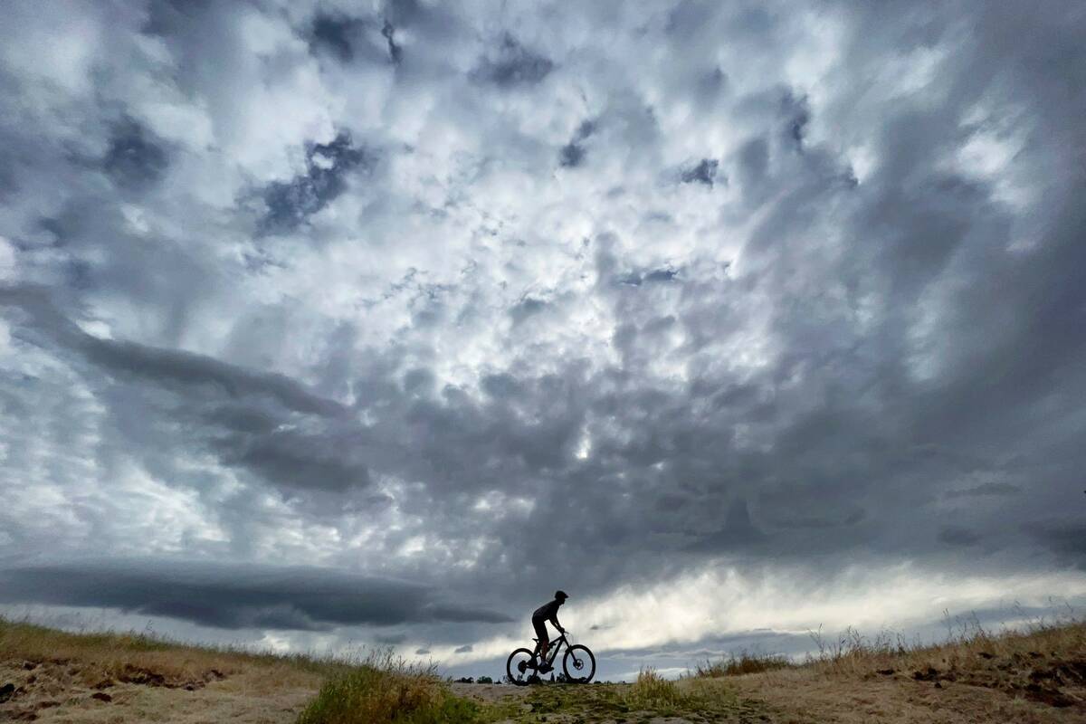 A bicyclist rides a mountain bike as storm clouds approach in the distance at Hidden Lakes Park ...