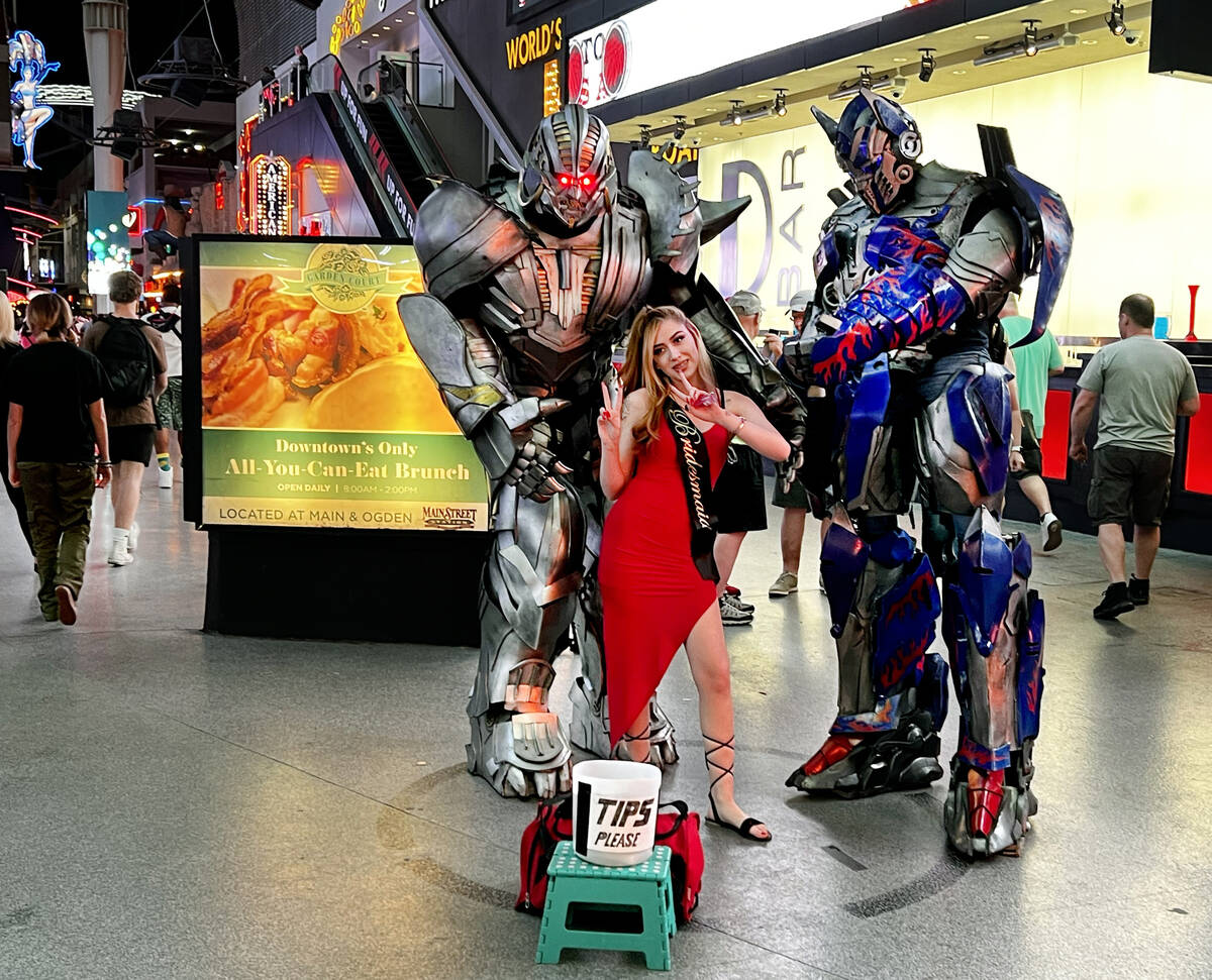 Street performers as Transformers pose with visitor Samantha Garcia within a designated circle ...