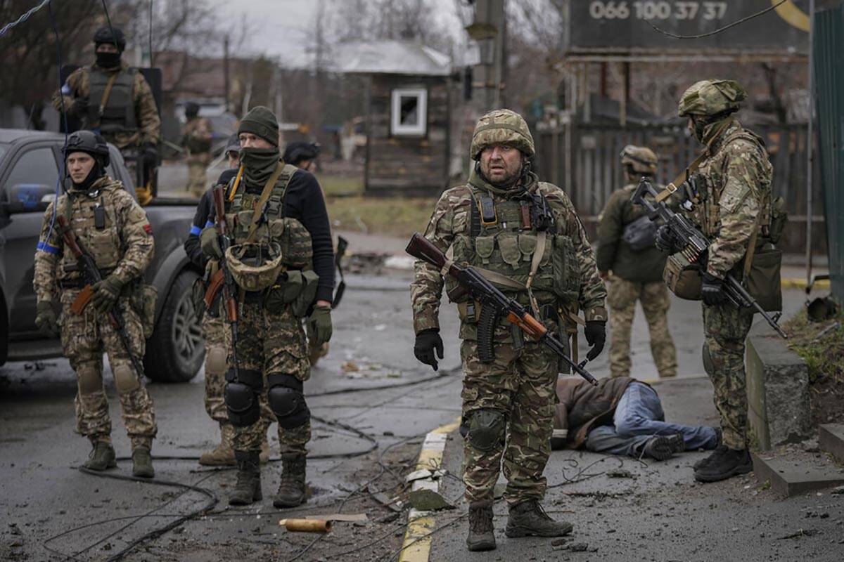 Ukrainian servicemen stand next to the body of man dressed in civilian clothing, in the formerl ...
