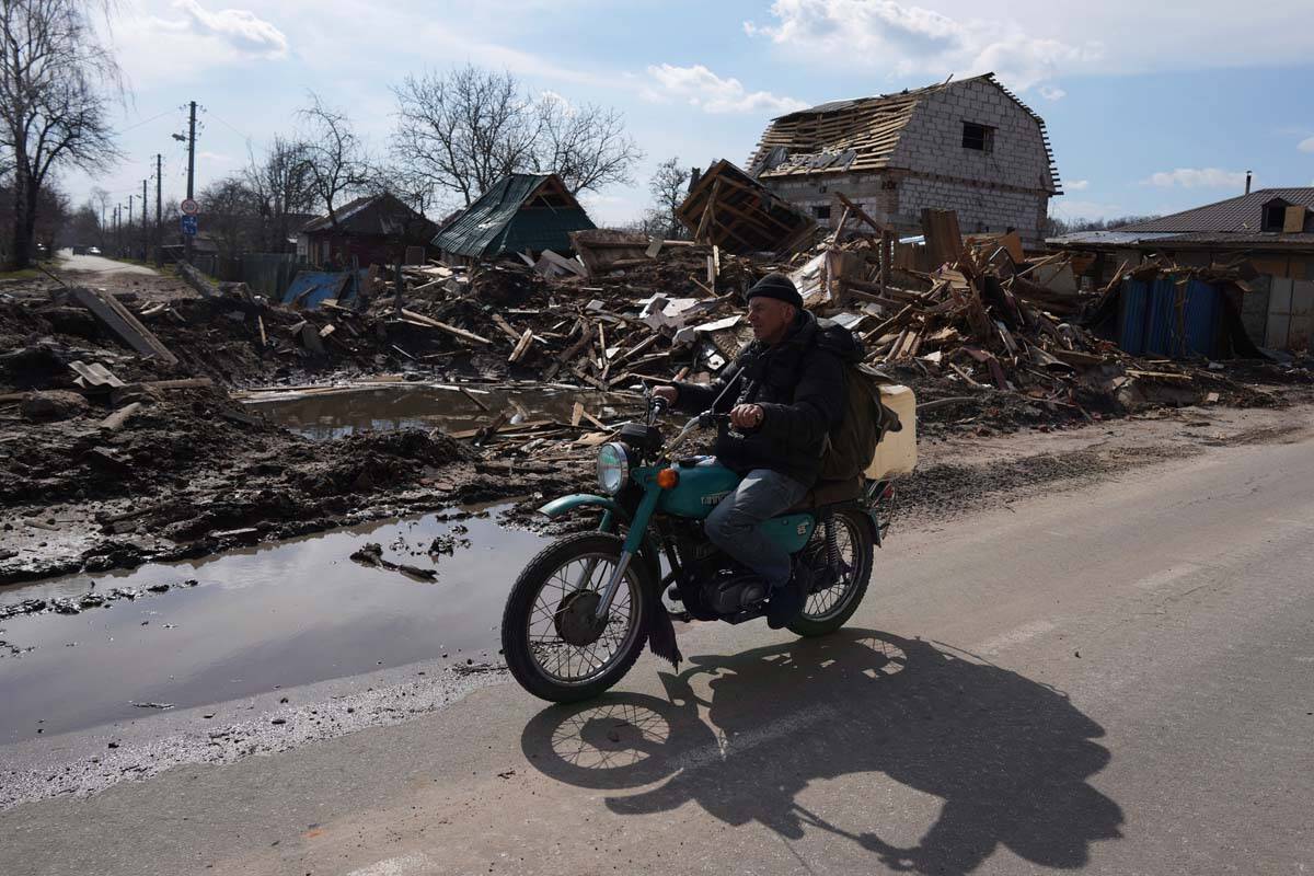 A man rides a motorbike past a house damaged by shelling in Chernihiv, Ukraine, Thursday, April ...