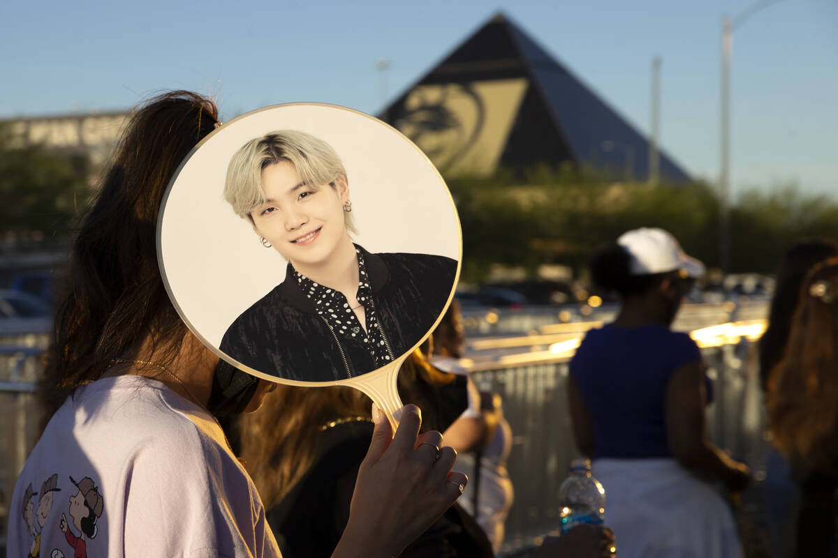A BTS fan shields themselves from the sun while walking into Allegiant Stadium for the Korean b ...