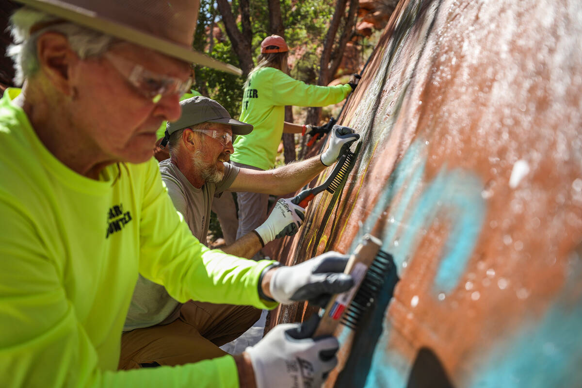 Volunteer Phil McKay, left, and Rick Momsen, center, work to remove graffiti along Ash Springs ...