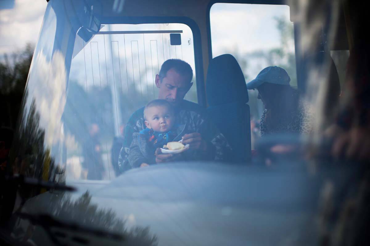 A man feeds a child as they arrive by bus at a reception center for displaced people in Zaporiz ...