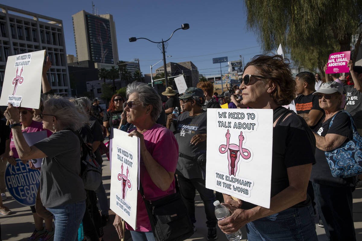 Attendees hold signs reading “we need to talk about the elephant in the womb” dur ...