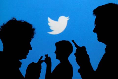 People holding mobile phones are silhouetted against a backdrop projected with the Twitter logo ...