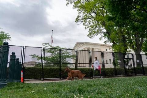A pedestrian with a dog walks past fencing that blocks off the area around the U.S. Supreme Cou ...