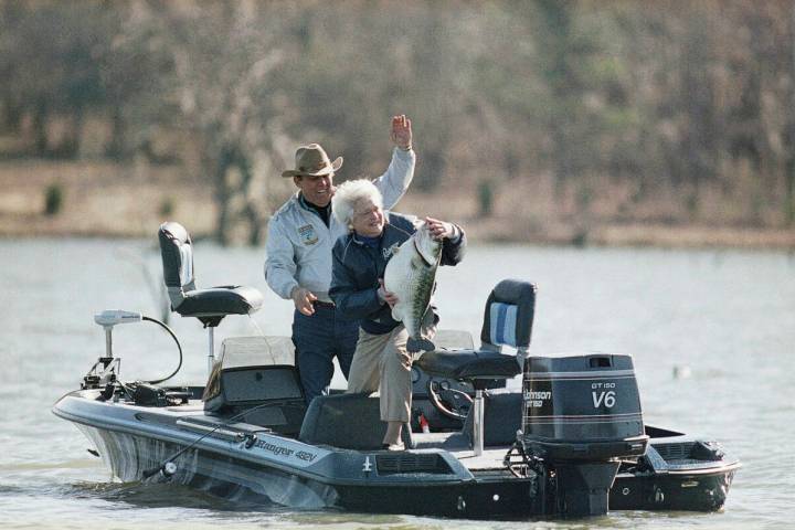First lady Barbara Bush holds a mounted bass as a joke with fishing partner Ray Scott at his la ...