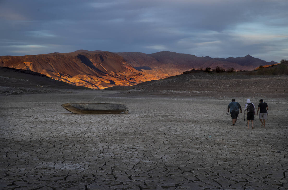 Fishermen walk past an old boat left behind as the waterline continues to recede about the clos ...