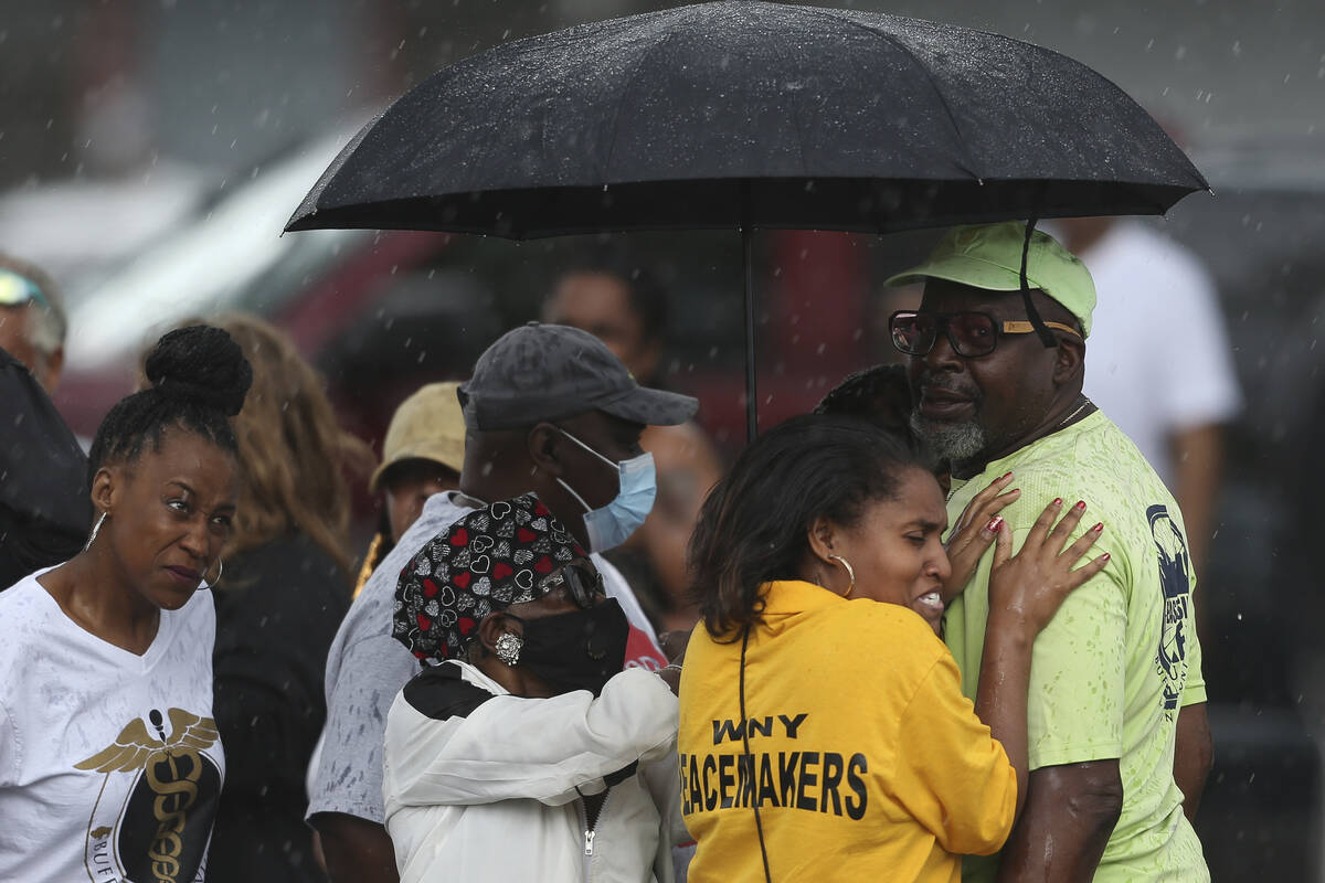 Bystanders gather under an umbrella as rain rolls in after a shooting at a supermarket on Satur ...