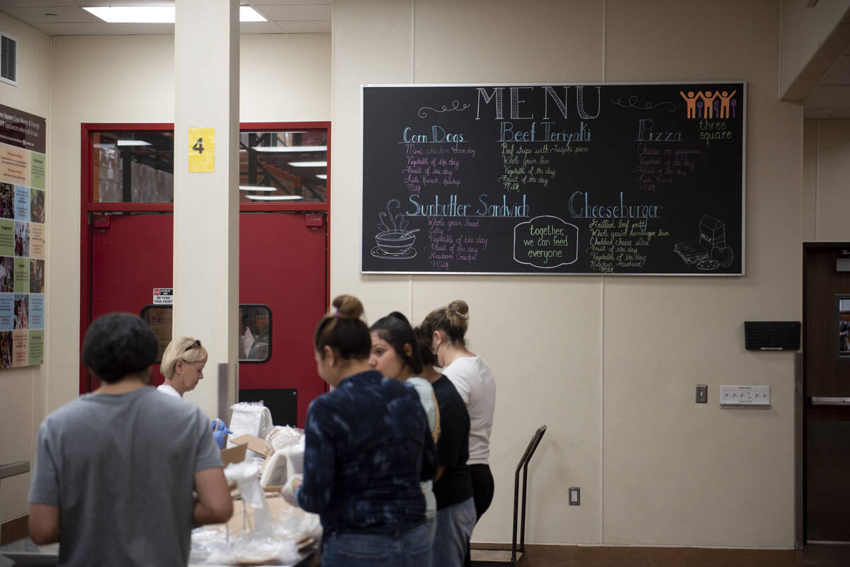 Volunteers help pack lunches for students on summer break at Three Square, the food bank servin ...