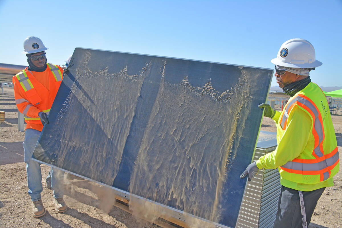 Electrician helpers Ronnie Graves, left, and Latwaun Elliott move and dust off a solar panel to ...