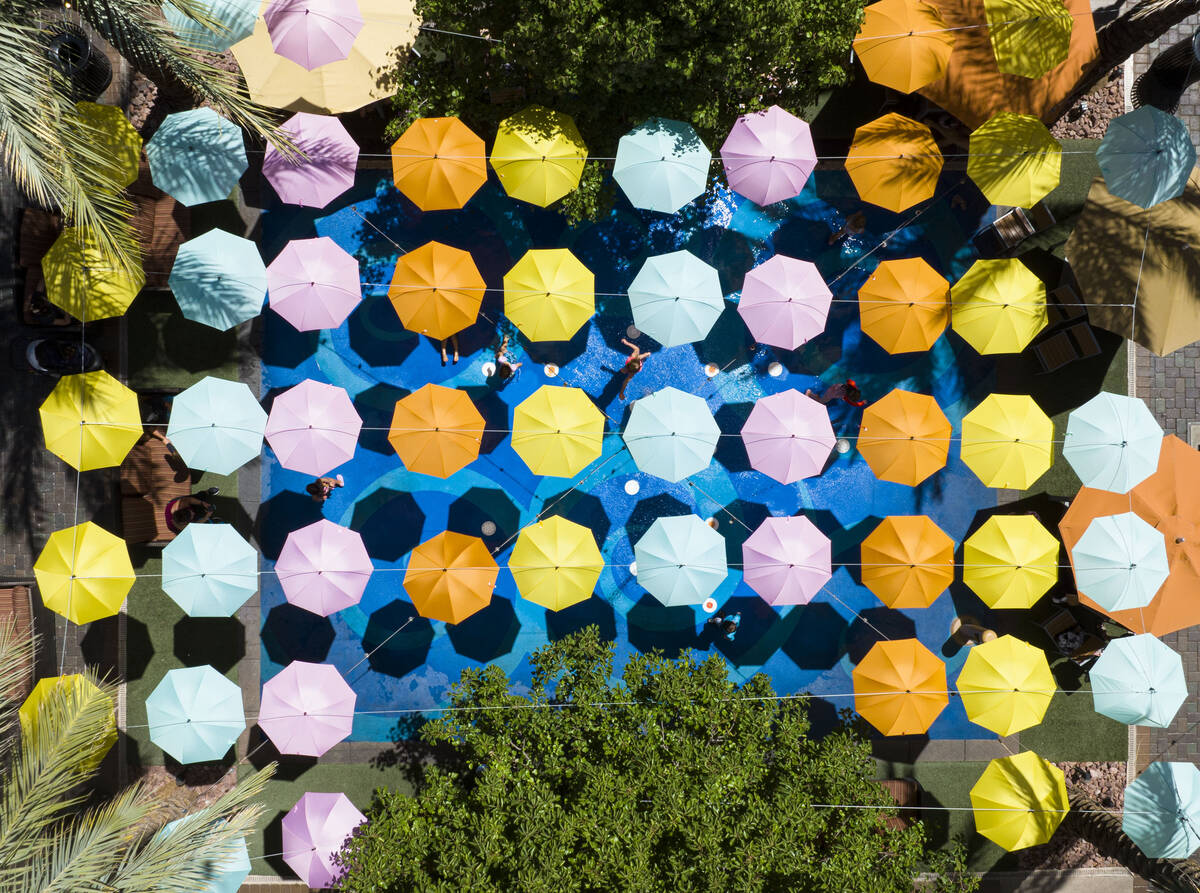Small umbrellas are hung over a splash pad as children cool themselves at The District on Thurs ...