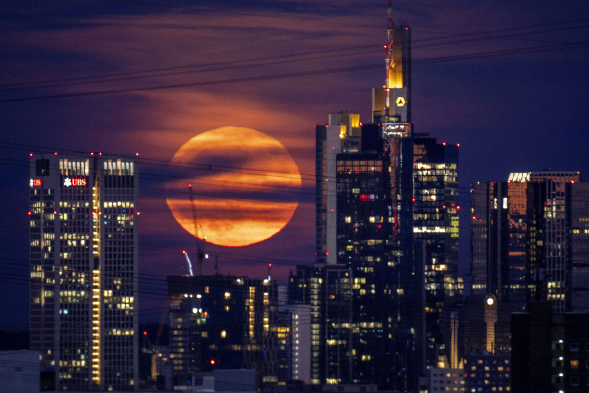 The full moon rises behind buildings in the banking district in Frankfurt, Germany, late Tuesda ...